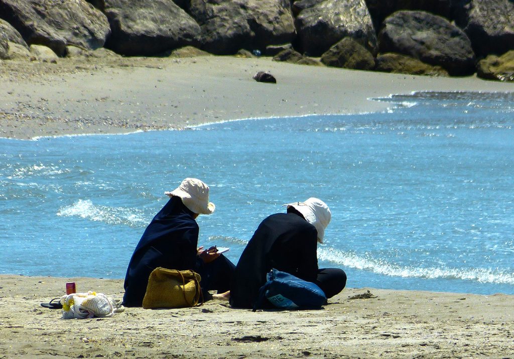 Photo de 2 personnes assises sur le sable face à la mer, en train de faire des croquis